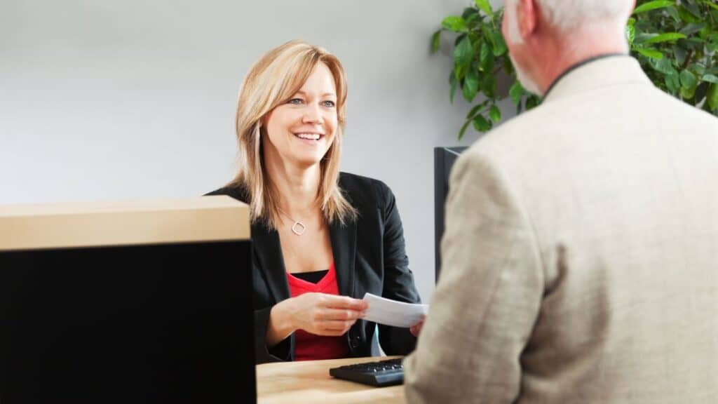 Elderly man speaking to the female teller at his bank.