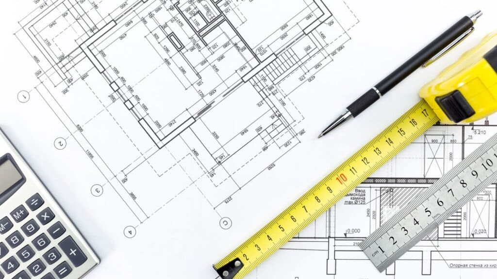 Creating a construction contract with building plans laid out on table with calculator, pen, tape measure, and ruler.